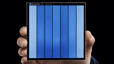 Microsoft Project Silica team member holding a coaster-sized square fused silica glass platter used for 4.8 TB long-term archival data storage.